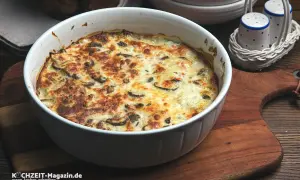 Herzhafter Kohlrabi-Auflauf mit Pilzen und Käse überbacken, serviert in einer weißen Auflaufform auf einem Holzbrett.