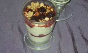 Dessert im Glas mit Kirschen, zerbröseltem Keks und Fruchtsauce.