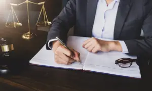 Prawnik przygotowuje wniosek o upadłość konsumencką, notując ważne szczegóły. Obok leżą okulary i młotek sędziowski.