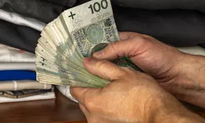 Dłonie trzymające plik banknotów 100 zł. To jeden z elementów, który wpływa na narzędzia polityki pieniężnej.