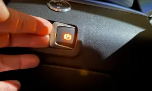 Dłoń naciska przycisk hamulca postojowego. Pytanie brzmi: na jakim biegu parkować, gdy ten przycisk jest aktywny?