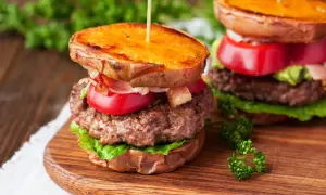 Pyszny burger na talerzu z soczystą wołowiną, chrupiącym bekonem, pomidorem i awokado, podany na słodkich ziemniakach.