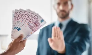 Ręka podaje plik banknotów 500 euro, mężczyzna w garniturze odrzuca je, co może symbolizować pozew o zapłatę.