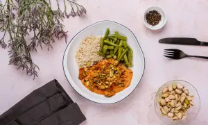 Talerz z ryżem, fasolką szparagową i kurczakiem w sosie z pistacjami. Obok naczynie z orzechami.