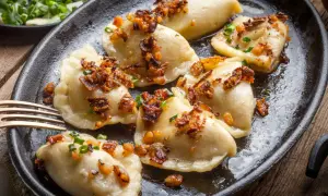 Pyszne pierogi z mięsem, polane skwarkami i posypane szczypiorkiem, na ciemnej patelni.