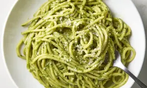 Pyszny makaron z pesto, posypany parmezanem, czeka na widelcu. Idealny na szybki obiad.