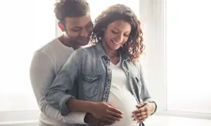 Un couple heureux, le futur papa enlace tendrement le ventre arrondi de sa compagne. Ils pensent déjà au prénom en N pour leur bébé.