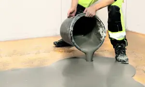 Arbetare häller jordfuktad betong från en hink för att jämna ut ett golv.