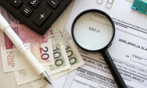 Pióro, banknoty, kalkulator i lupa nad deklaracją VAT-7. Przygotowanie do rozliczenia podatku.