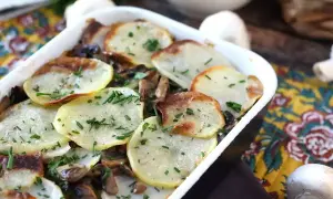 Zapiekanka ziemniaczana z pieczarkami, posypana szczypiorkiem, w białym naczyniu.