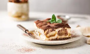Une part de tiramisu onctueux, saupoudrée de cacao, garnie de menthe fraîche. Parfait pour une recette tiramisu réussie.