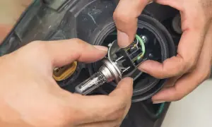 Wymiana żarówki przód Opel Corsa C. Dłonie montują nową żarówkę w reflektorze.
