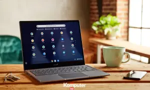Laptop z systemem Chrome OS na drewnianym stole, obok kubek i telefon. Ikony aplikacji Google widoczne na ekranie.