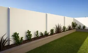 Nowoczesne ogrodzenie betonowe wzory, z prostymi liniami i minimalistycznym designem, otacza zadbany ogród z zieloną trawą i roślinnością.