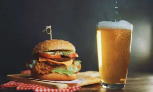 Un succulento hamburger con formaggio fuso e lattuga, accompagnato da una birra bionda spumeggiante.