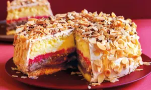 Una fetta di pizza dolce abruzzese, con strati di crema, cioccolato e confettura, ricoperta di mandorle tostate e panna.