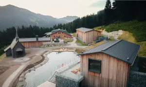 Idyllische hotels auf dem berg mit kleinem See und Kapelle, umgeben von Wald und Bergen.