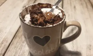 Un delizioso mug cake al cioccolato, appena sfornato, con cuore e scritta "chocolate" sulla tazza, spolverato di zucchero a velo.