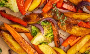 Un assortiment coloré de légumes rotis au four : carottes, pommes de terre, brocolis et oignons rouges, parsemés de thym frais.