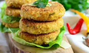 Złociste kotlety z kalafiora, chrupiące i aromatyczne, ułożone na sałacie. Obok czerwone i żółte papryczki chili.