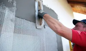 Obrero aplica mortero sobre malla de refuerzo para asegurar la durabilidad de la fachada.