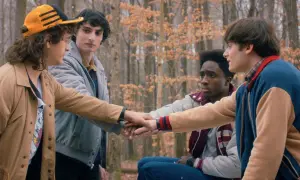 Czterech przyjaciół z Stranger Things w lesie, łączących dłonie.