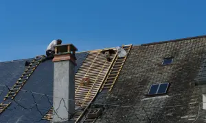 Un couvreur travaille sur un toit en ardoise, en cours de rénovation. Ces gros travaux pourraient ouvrir droit à une déduction fiscale pour le nu-propriétaire.
