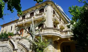 Élégante villa abandonnée sur la Côte d'Azur, avec un grand escalier en pierre et un cactus imposant devant sa façade ornée.