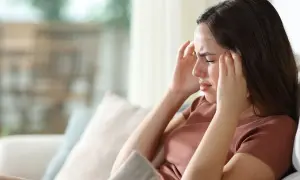 Kobieta zamyka oczy, masując skronie. To wyraźne objawy stresu, które mogą dotknąć każdego.