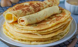 Ein Stapel goldbrauner Eierkuchen, zwei davon gerollt, warten auf ein leckeres Eierkuchen Rezept.