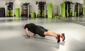 Mężczyzna wykonuje pompki na triceps w siłowni. W tle widać sprzęt treningowy.