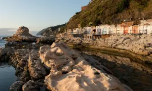 Scogliere rocciose e cabine colorate sulla spiaggia del Passetto, illuminate dalla luce dorata del tramonto.