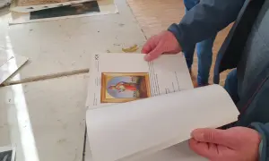 Hände halten ein Buch mit einem Bild eines Heiligen. Ein Detail der Kunstrestauration.