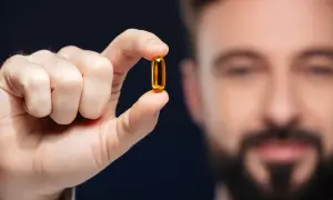 Mężczyzna trzyma kapsułkę z olejem rybim, bogatym w kwasy omega 3.