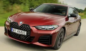 Czerwone BMW M440i z charakterystycznym grillem pędzi po drodze, kierowca w okularach przeciwsłonecznych.