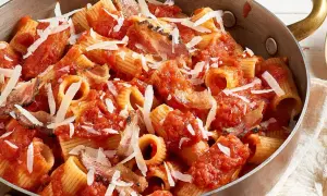 Rigatoni all'amatriciana dans une poêle en cuivre, garni de copeaux de parmesan. Un plat réconfortant et savoureux.