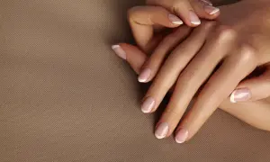Dłonie z idealnym frenczem, podkreślającym naturalne kolory paznokci. Delikatny manicure na beżowym tle.