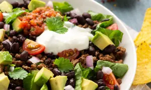 Ein bunter Taco Salat mit Hackfleisch, schwarzen Bohnen, Avocado, Tomaten, Zwiebeln und einem Klecks Sauerrahm. Perfekt für einen leichten Genuss.