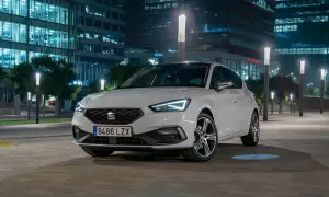 Blanco Seat León aparcado de noche frente a edificios modernos. Las luces LED del coche y las farolas crean un ambiente urbano. Opiniones sobre este modelo son muy positivas.