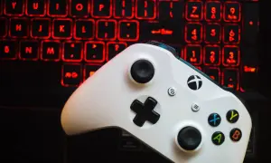 Biały kontroler Xbox One na tle podświetlanej na czerwono klawiatury.