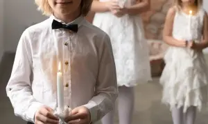 Dzieci w białych strojach trzymają zapalone świece podczas Komunii Świętej.