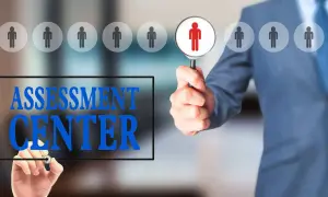 Uomo in giacca blu esamina candidati con lente d'ingrandimento. Testo "ASSESSMENT CENTER" scritto su schermo.