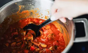 En hand rör i en gryta med mustig coq au vin, fylld med kyckling, svamp och grönsaker i en rik sås.