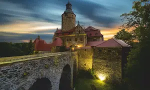 Zamek Czocha, gdzie jest, w blasku zachodzącego słońca i nocnych świateł, z kamiennym mostem i wieżą.