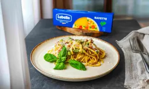 Pyszna carbonara ze szparagami na talerzu, udekorowana bazylią. Obok opakowanie makaronu Lubella Bavette.
