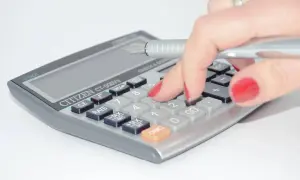 Mano con unghie rosse preme tasti di una calcolatrice per la ripartizione spese condominiali.
