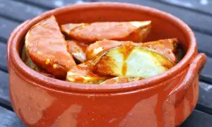 Patatas bravas, pommes de terre croustillantes nappées d'une sauce épicée, servies dans un plat en terre cuite.
