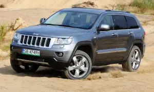 Szary Jeep Grand Cherokee 3.6 pokonuje piaszczysty teren, wzbijając tumany kurzu.