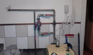 Montaż pompy CO w układzie otwartym. Widoczna instalacja miedziana, czerwona pompa obiegowa, zawory i fragment kotła.