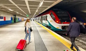 Kobieta z czerwoną walizką czeka na pociąg na stacji Palermo lotnisko.